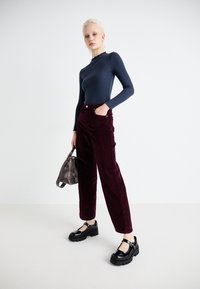 Mornarsko plavi rebrasti top dugih rukava uparen s bordo kord pantalona širokih nogavica. Model nosi debele crne lakirane cipele i drži malu sivu torbu.