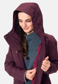 Giacca isolata bordeaux con cappuccio, zip frontale e tasche laterali; presenta una texture morbida, fodera interna a contrasto e polsini regolabili.