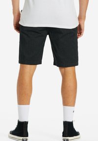 Shorts in denim scuro a taglio dritto, che si fermano appena sopra il ginocchio. Abbinati a calze bianche alla caviglia e sneakers alte nere.