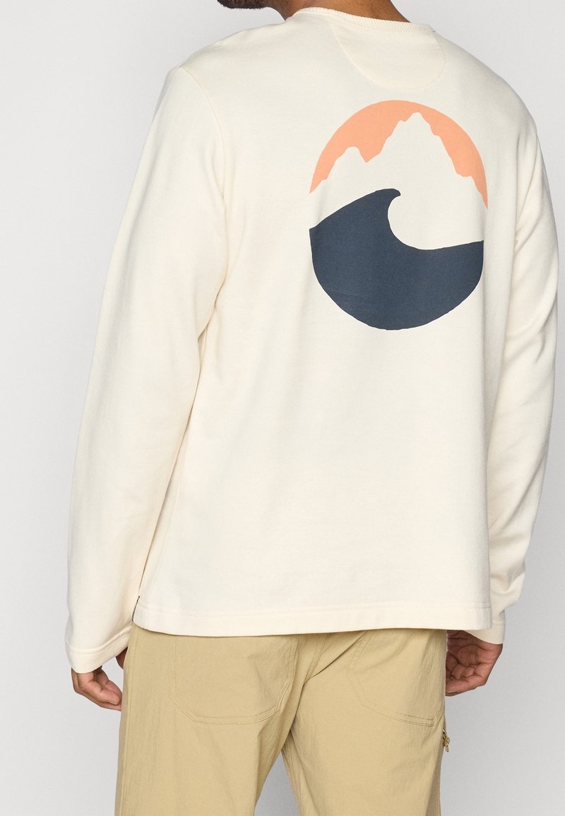 Kermaankermanvärinen collegepaita, jossa on pyöreä kuvio, jossa on persikanvärisiä vuoria ja tummansininen aalto. Pitkät hihat ja pyöreä kaula-aukko.