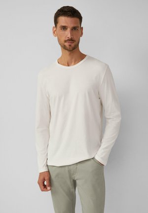 Langärmliges Creme-T-Shirt aus weichem Stoff mit rundem Halsausschnitt, kombiniert mit hellgrünen Hosen mit lockerer Passform.