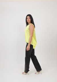 Gul satin top med prikket nederdel, der er kort foran og længere bagpå, kombineret med sorte faux læderbukser og nude højhælede sandaler på en model.