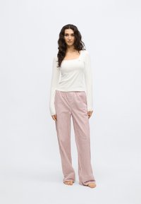 Bijela majica dugih rukava s kvadratnim izrezom u kombinaciji s vrlo širokim hlačama svijetloružičaste boje s prugastim uzorkom. Mekani materijal s elastičnim strukom.