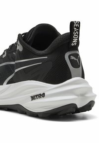 Czarne sportowe buty na płaskiej podeszwie z przewiewną siateczką, srebrnymi akcentami, grubą białą podeszwą środkową i czarną teksturowaną podeszwą zewnętrzną. Posiadają pętelkę do zakładania.