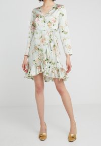 Vestito avvolgente floreale di colore verde chiaro con maniche lunghe, orlo a volant e vita con fiocco. Caratterizzato da una stampa di fiori rosa e arancioni su un tessuto liscio.