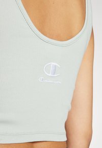 Mintgrønn ribbestrikket crop-top med bred utringning, med en hvit brodering på logoen foran. Materialet ser ut til å være elastisk og tettsittende.