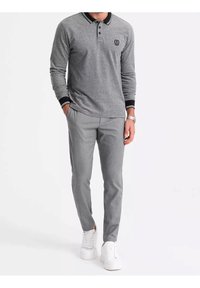Polo à manches longues gris avec col rayé noir et blanc, assorti à un pantalon slim gris clair et des baskets blanches.