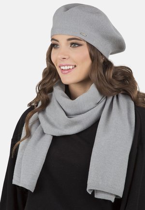 Grå strikket baret med en glat tekstur og sølvhardware, parret med et matchende gråt ribbet tørklæde, båret over en sort top.