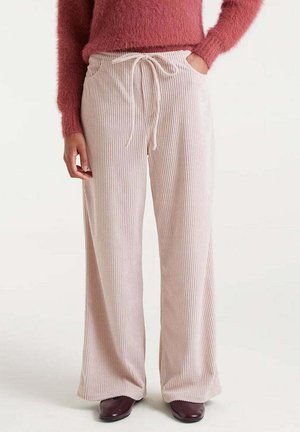 Pantalones de corte ancho de sarga en un rosa claro, con cintura ajustable y textura de costillas verticales, combinados con un suéter rosa peludo y zapatos oscuros.