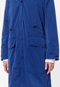 Blå, lång ytterjacka gjord av slätt, vattenavvisande material med två frontfickor, justerbar dragsko i midjan och knäppning.