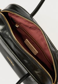 Bolso de mano de cuero negro con acabado brillante, cremallera dorada y interior de tela burdeos. Cuenta con una etiqueta de la marca y bolsillos adicionales con cremallera en el interior.