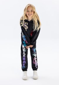 Zwarte sweatshirt en joggers met kleurrijke grafische tekst en ontwerpen. De stof lijkt zacht, met ribgebreide boorden en een ontspannen pasvorm.