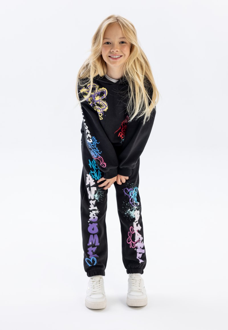 Sweatshirt noir et jogging avec des textes et des designs graphiques colorés. Le tissu semble doux, avec des poignets côtelés et une coupe décontractée.