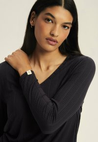 Black v-neck long-sleeve top with textured ribbed fabric. Model wears a gold-tone hoop earring and a bracelet with a small square accent.