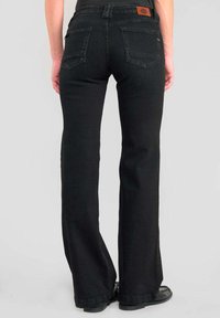 Jeans negros acampanados con una textura suave, que cuentan con un parche de piel marrón en la cintura trasera y dos bolsillos traseros.