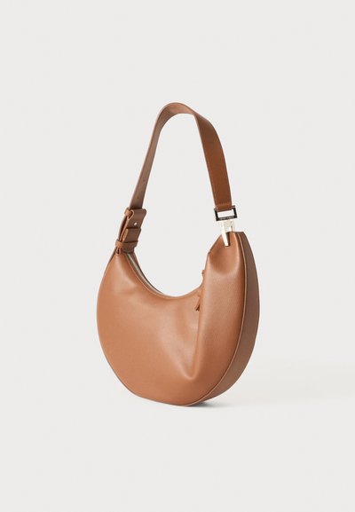 Sac à main en cuir marron en forme de croissant avec une large bandoulière réglable et une fermeture éclair sur fond uni.