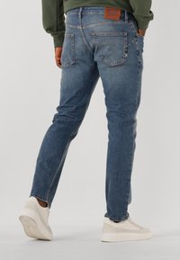 Jeans in denim blu medio con vestibilità slim, caratterizzati da tasche posteriori e un'etichetta in pelle sulla vita. Abbinati a sneakers beige.