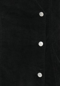 Tissu en velours côtelé noir présentant un motif à côtes verticales, avec des boutons-pression argentés comme accents matériels le long de l'avant.