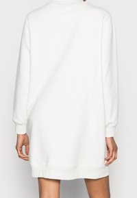 Vestito felpa bianco con maniche lunghe, polsini a costine e orlo arrotondato. Texture liscia, vestibilità comoda, design minimalista.