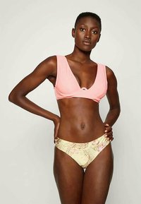 Biquíni de duas peças com um top cropped rosa suave com alças largas e um decote baixo, combinado com partes de baixo amarelas adornadas com um padrão floral de palmeiras.