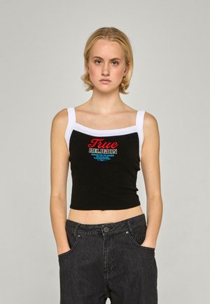 Black cropped tank top with white straps featuring red and blue embroidered text. Paired with high-waisted black jeans.