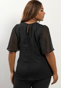Blusa nera con maniche corte a palloncino trasparenti. Presenta una sottile texture a righe verticali e un piccolo apertura a forma di chiave sul retro.
