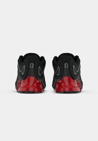 Crne sportske cipele s crvenim gumenim potplatima, teksturiranim gornjim dijelom od mrežice, istaknutim zakrivljenim dizajnom i reflektirajućim akcentima na području pete.