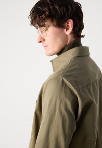 Olive green jacket with a collared neckline and textured fabric, featuring a snug fit and minimalistic design.