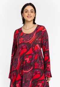 Robe longue à manches longues rouge avec un motif floral abstrait dans des nuances variées de rouge, violet et noir. Tissu doux avec un col rond.