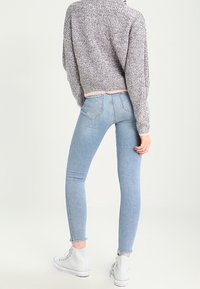 Jasnoniebieskie wąskie dżinsy z postrzępionym dołem, w połączeniu z szarym swetrem o teksturowanej fakturze i białymi trampkami za kostkę.