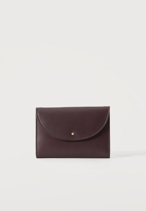 Portefeuille en cuir marron foncé avec rabat incurvé et petite fermeture à bouton doré, présenté sur un fond gris clair.
