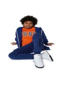 Chándal azul marino con una camiseta naranja de DKNY y zapatillas de caña alta blancas. El chándal tiene detalles de logo y una sudadera con cremallera.