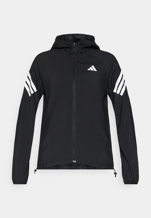 Schwarze Windjacke mit Kapuze, versehen mit weißen Drei-Streifen-Akzenten auf den Ärmeln und einem Reißverschluss vorne, aus leichtem Stoff gefertigt.