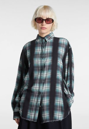 Plaid button-up shirt in teal, black, and white; long sleeves; relaxed fit; frayed hem; features large check pattern.