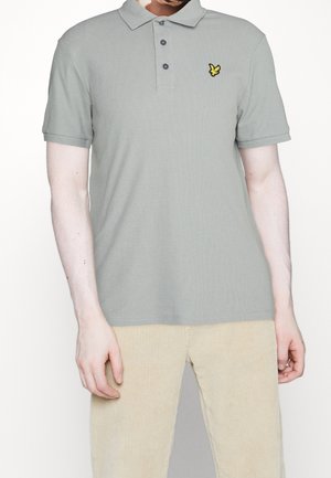 Hellgraues Baumwoll-Poloshirt mit kurzen Ärmeln, drei Knöpfen und gesticktem gelbem Logo auf der linken Brust. Strukturierter Stoff.