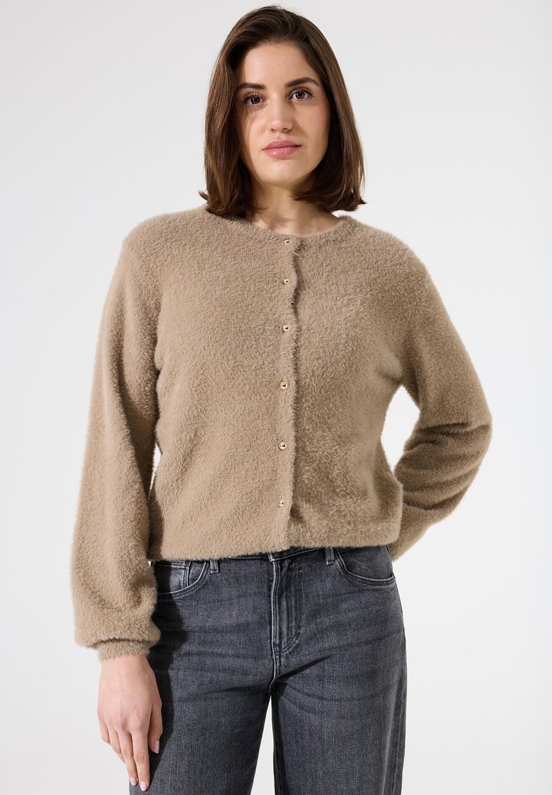 Cardigan beige à boutons fabriqué à partir d'un matériau moelleux et texturé. Il présente des manches longues et des boutons dorés sur le devant.