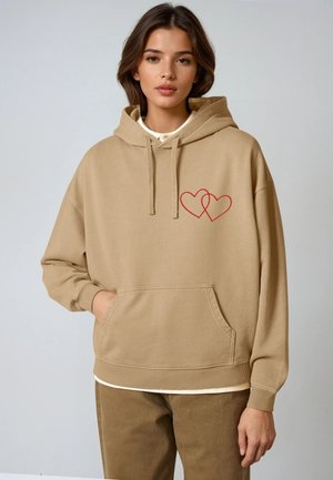 Beige hoodie gemaakt van zachte stof, met een voorzak en een rood hartontwerp. Oversized pasvorm met trekkoorden in de capuchon.