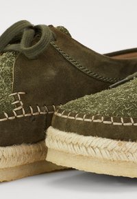 Espadrilles vert olive avec un dessus en daim et texturé. Caractéristiques des accents cousus et une semelle intermédiaire en jute avec une base douce. Design à bout rond.