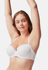 Soutien-gorge blanc rembourré avec des bretelles fines réglables et un design sans coutures. Présente une fermeture à crochets et une texture lisse et douce.