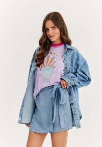 Džínová bunda, světle modré tričko s grafikou a designem lotosu a odpovídající modré krátké kalhoty s obvazem. Hladké textury; uvolněný střih.