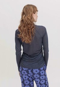 Langärmliges, dunkelgraues Oberteil mit lockerer Passform, kombiniert mit blauen Leggings im Blumenmuster. Texturierten Stoff sorgt für Weichheit.