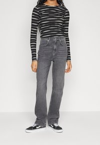 Svart- och vitrandig långärmad topp ihop med högmidjade grå denimjeans och svarta låga sneakers. Slät tyg, figurnära design.