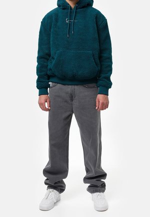 Sudadera de forro polar en color verde azulado con bolsillo tipo canguro y capucha con cordón, combinada con jeans grises de corte holgado y zapatillas blancas. Textura suave y diseño informal.
