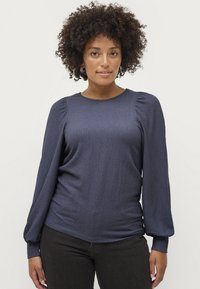 Marineblå, struktureret langærmet top med pufærmer og rund hals, parret med mørke jeans. Blødt stof med subtile mønsterdetaljer.