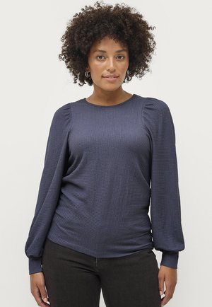 Marineblå, struktureret langærmet top med pufærmer og rund hals, parret med mørke jeans. Blødt stof med subtile mønsterdetaljer.