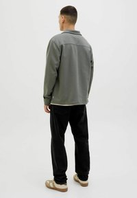 Gray fleece jacket with a collar, relaxed fit, and long sleeves. Paired with black tapered pants and beige sneakers. Minimalist design.