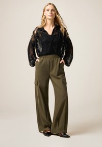 Zwarte kant blouse met lange mouwen, gecombineerd met olijfgroene cargo-broek met wijde pijpen en zijzakken. Zwarte flats met spitse neuzen.