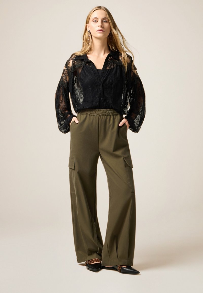 Zwarte kant blouse met lange mouwen, gecombineerd met olijfgroene cargo-broek met wijde pijpen en zijzakken. Zwarte flats met spitse neuzen.