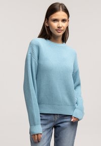 Jasnoniebieski sweter dzianinowy z okrągłym dekoltem, ściągaczami na rękawach i luźnym fasonem. Połączony z dżinsami, prezentuje swobodny styl.
