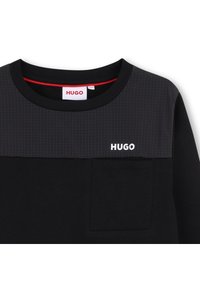Maglietta nera a maniche lunghe con yoke a motivo a griglia, taschino sul petto e accento rosso all'interno del collo. Logo "HUGO" in bianco.